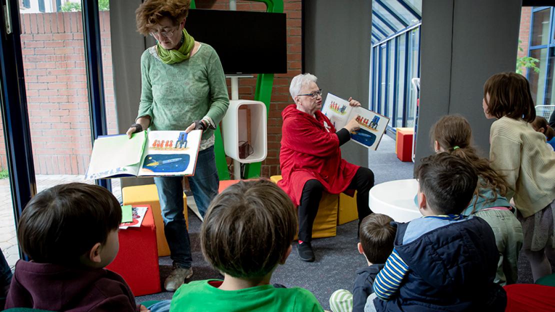 Motiv des "Vielfalt bewegt Frankfurt"-Kalenders für November 2024: Zwei Omas gegen rechts lesen Kindern aus Kinderbüchern vor und reden dabei über Alltags-Diskriminierung.