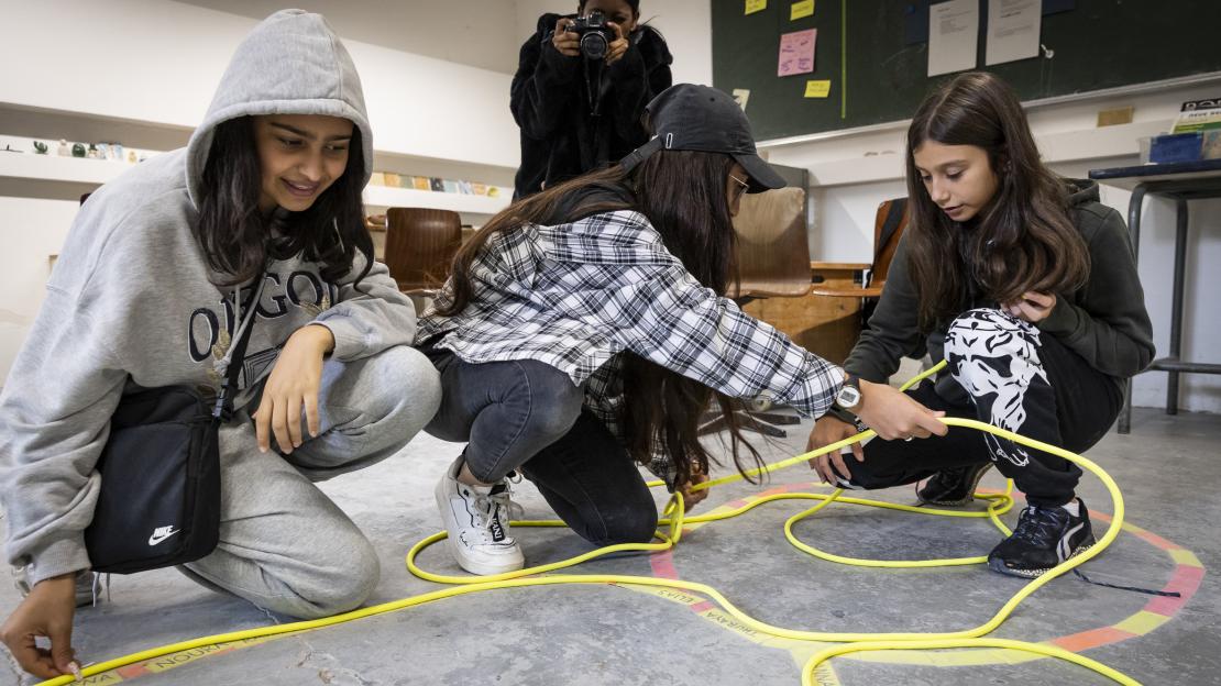 Motiv des "Vielfalt bewegt Frankfurt"-Kalenders für September 2024: Schülerinnen bei einem Film-Workshop des Vereins Hoch 9 kniend auf dem Boden.