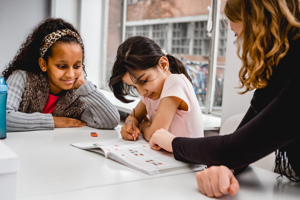 Eine Pädagoging am Tisch mit zwei Mädchen bei Schreibübungen