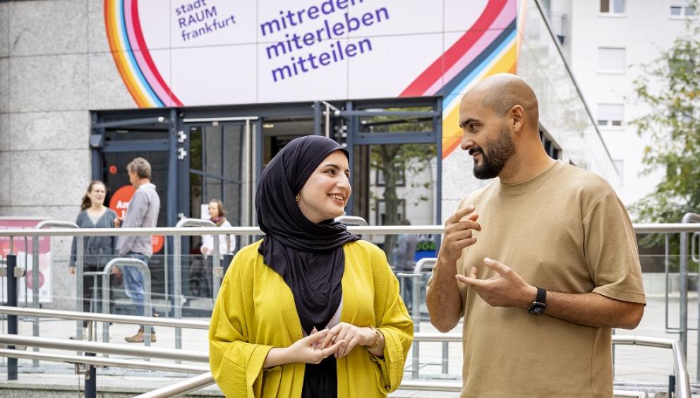 Ein Mann und eine Frau unterhalten sich vor dem Eingang zum Stadtraumfrankfurt