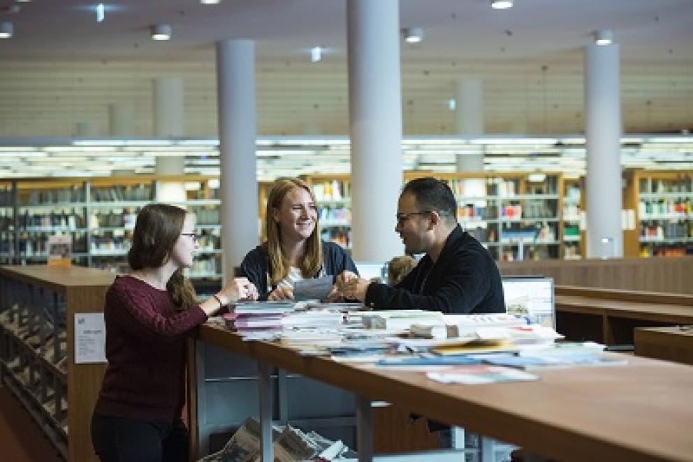 Zwei Frauen und ein Mann unterhalten sich in einer Universitätsbibliothek